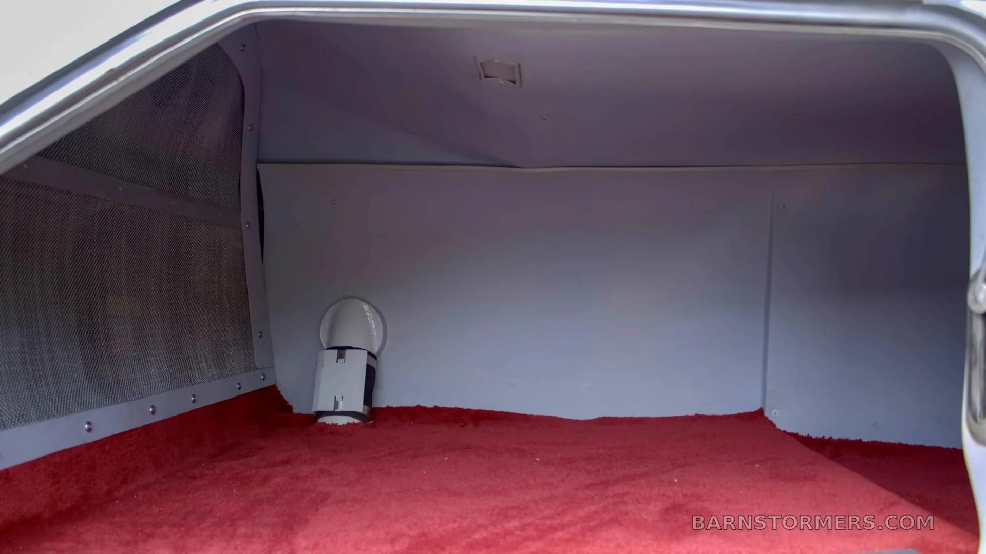An empty aircraft baggage compartment with a red carpeted floor and light gray walls.
