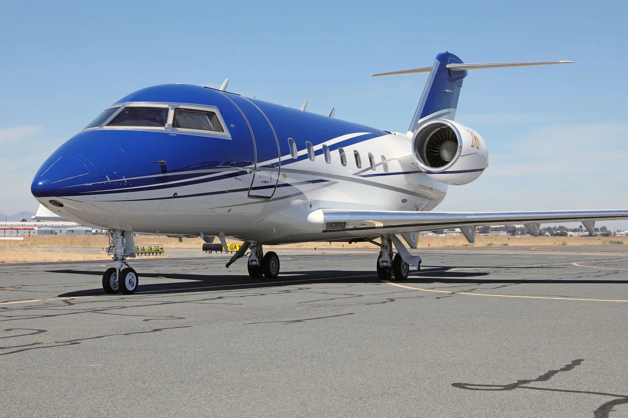 A close-up view of the front-right of the blue and white Bombardier Challenger 604 aircraft (N436DM) on a tarmac.
