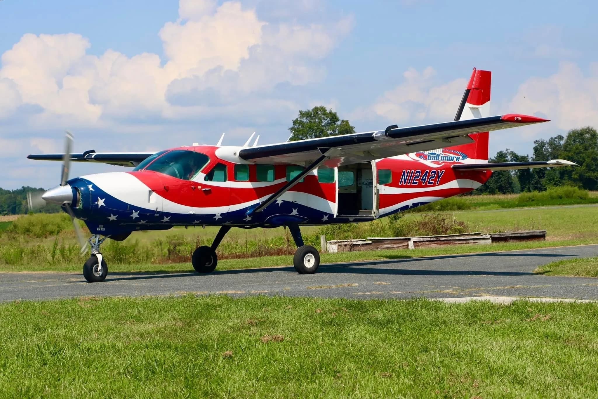 A Cessna Caravan aircraft with a patriotic paint scheme parked on a grassy airfield.