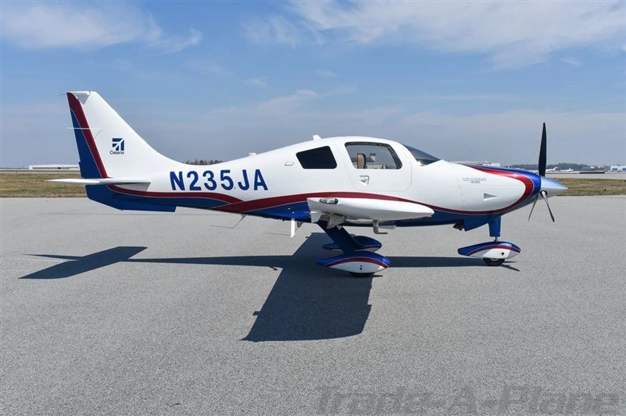 A white, blue, and red Cessna 400 aircraft with tail number N235JA is parked on an asphalt tarmac under a blue sky.