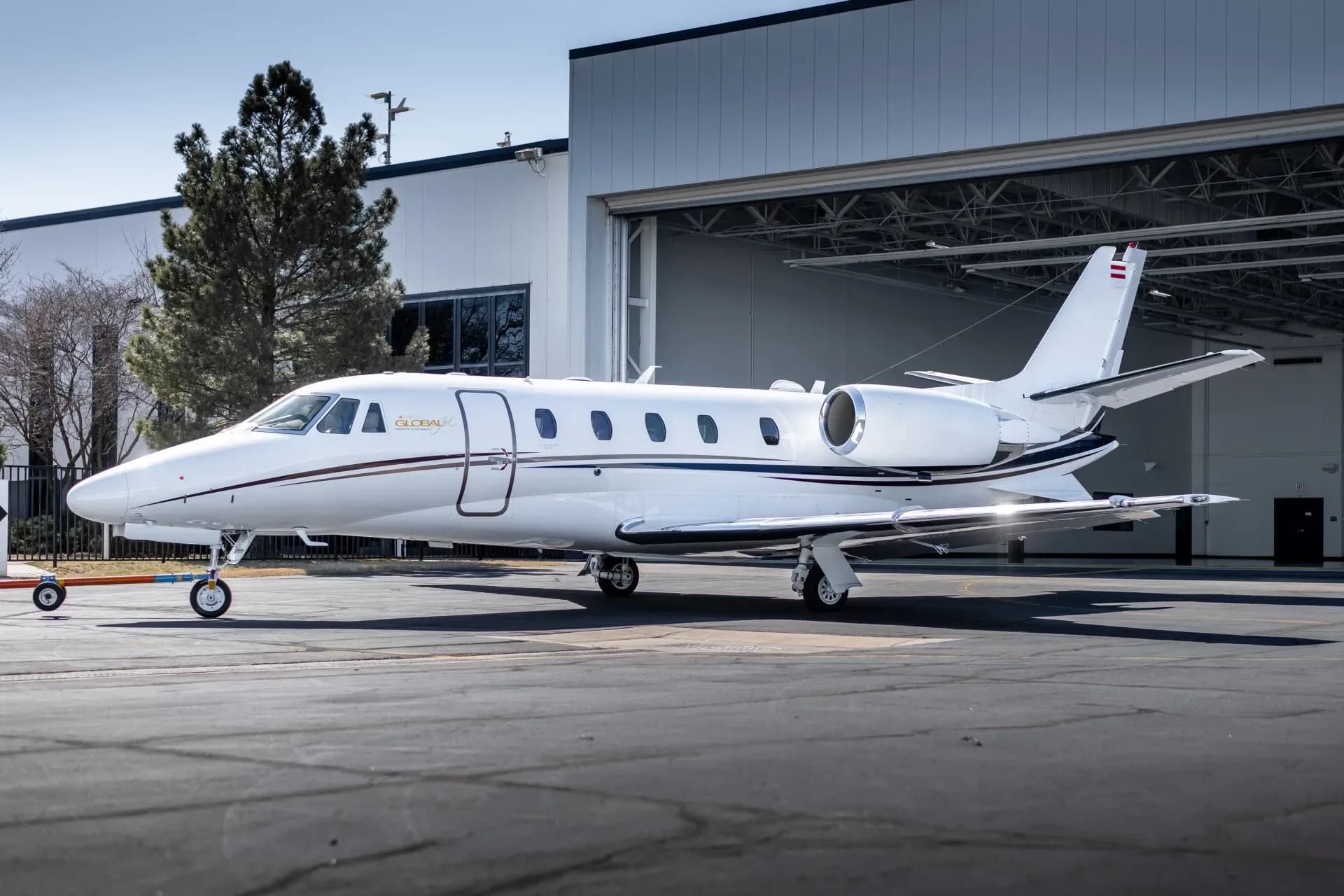 A white business jet with dark blue and gold stripes parked on an asphalt apron in front of a hangar.