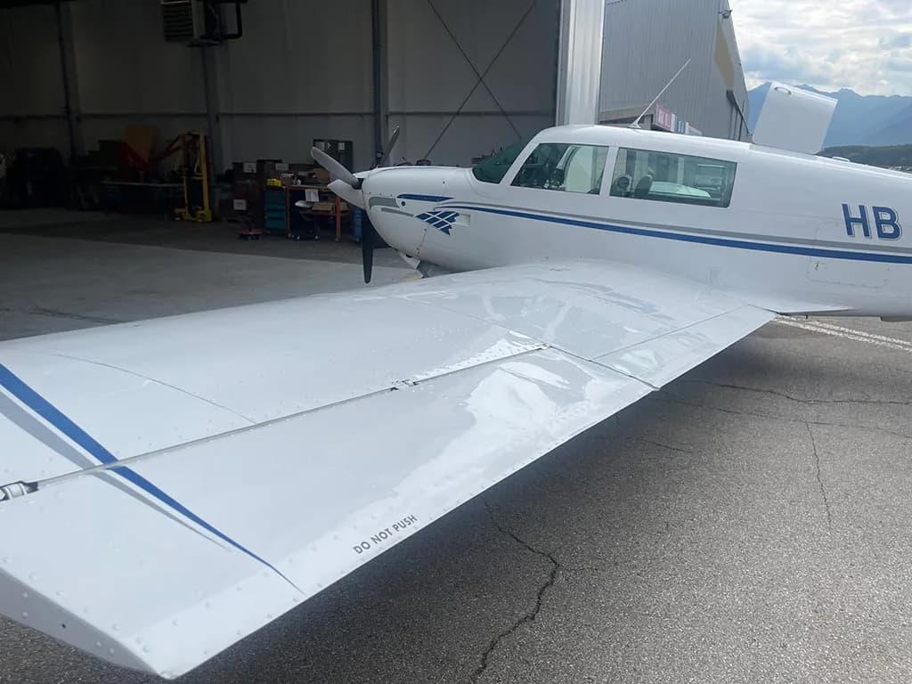 Top view of the wing and fuselage of a white aircraft with blue stripes, parked inside a hangar.