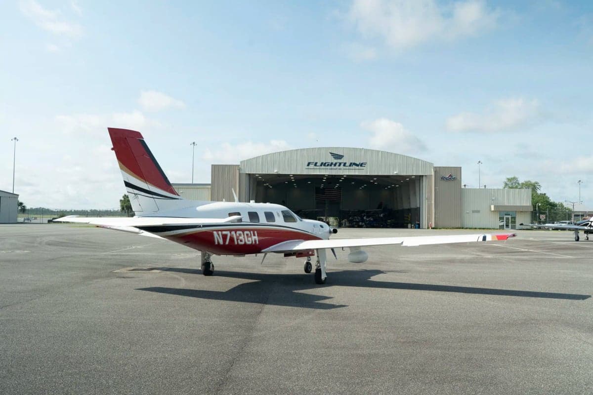 A white and red Piper M500 aircraft with registration N713GH parked on an asphalt tarmac in front of a Flightline hangar.