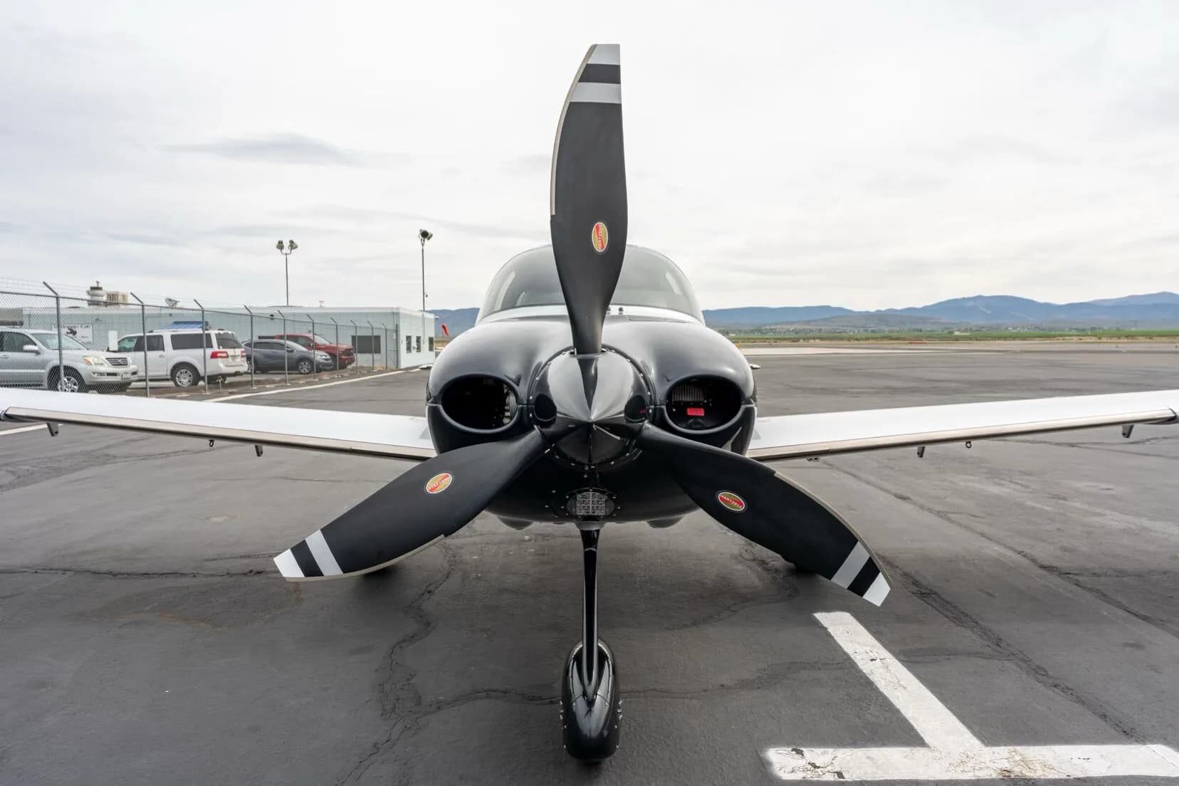 Front view of a black, blue, and silver single-engine aircraft with a three-bladed propeller on an airfield.