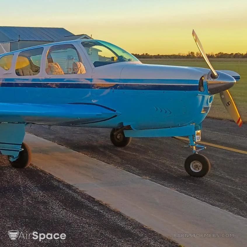 A light blue and white single-engine aircraft with a propeller, parked on a tarmac at sunset.