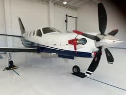 A TBM 930 aircraft is parked inside a hangar, showcasing its white and blue paint scheme.