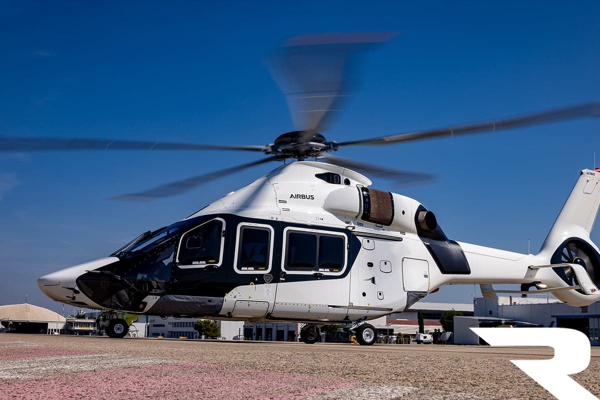 A white and black Airbus H160 helicopter sits on a helipad under a clear blue sky.