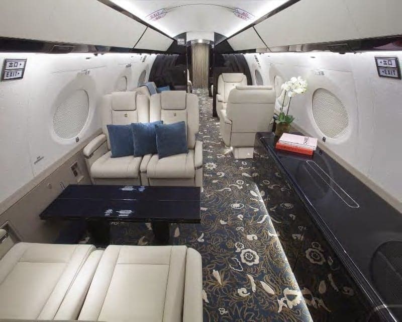 Aircraft interior with seats, tables, and floral carpet.