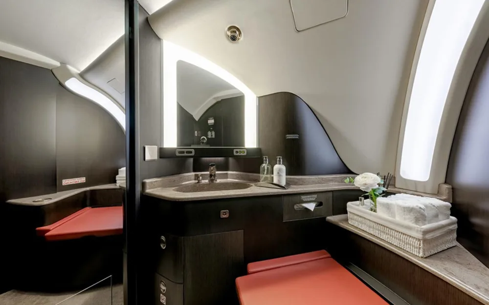 A modern aircraft lavatory with a dark wood vanity, a lighted mirror, and a red toilet seat.