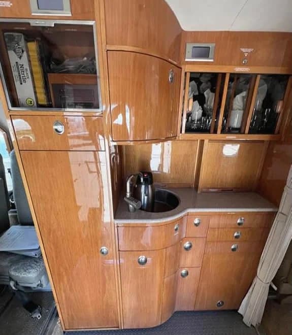 A galley area with wood cabinetry, a sink, and storage compartments inside the aircraft.