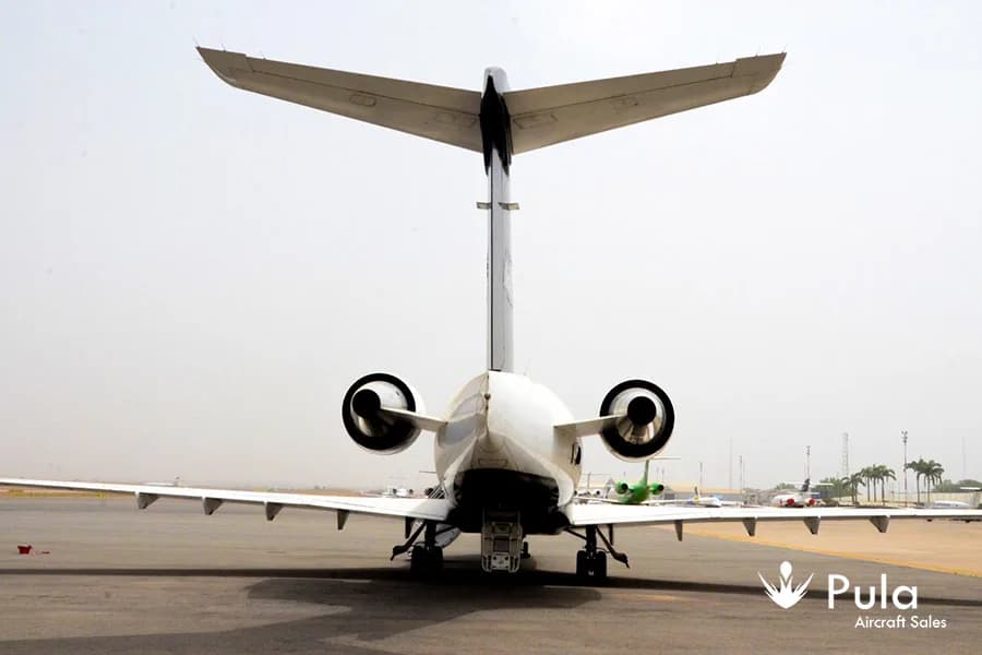 A rear view of a white and black Bombardier Challenger 604 business jet (N64JS) on a tarmac.