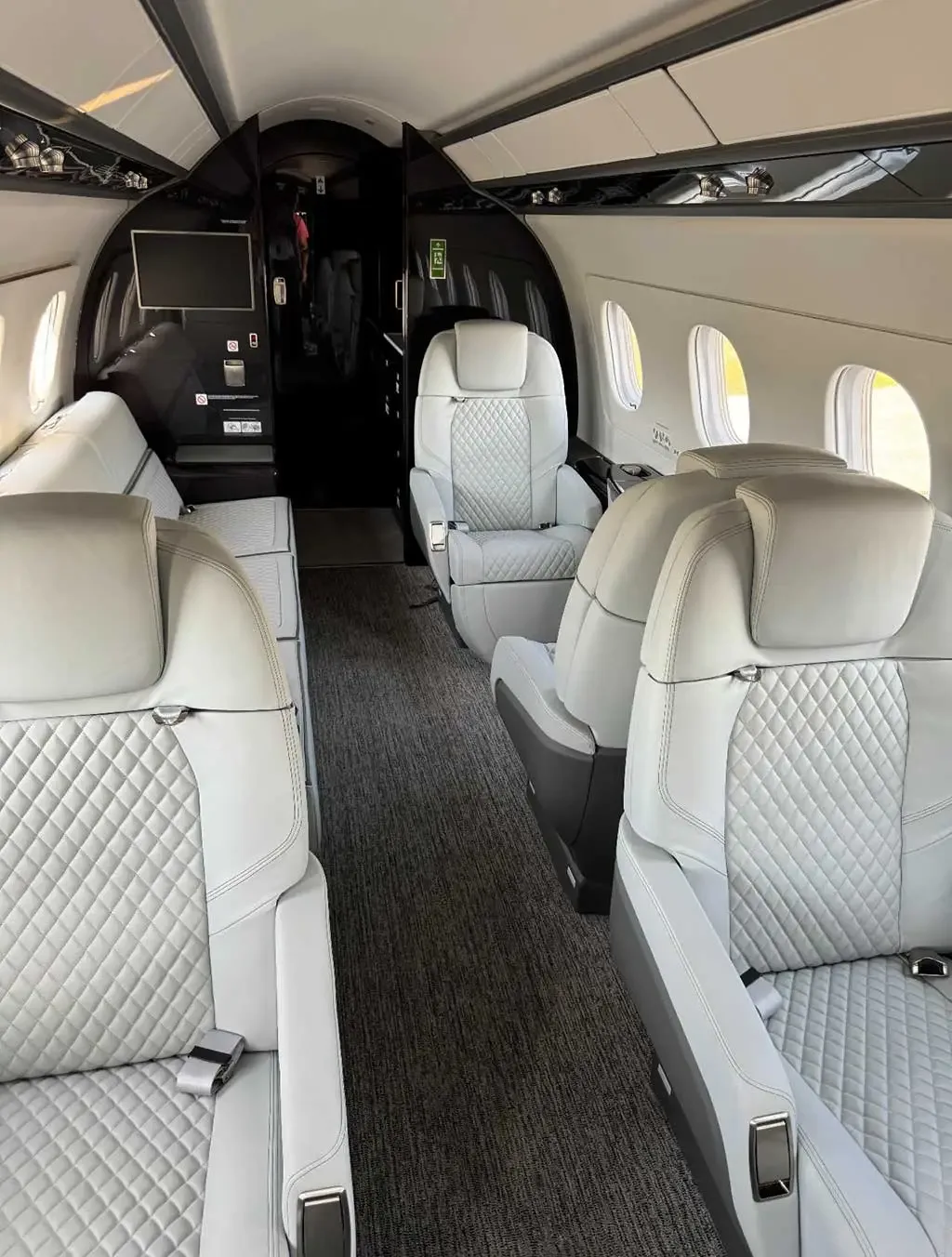 A view inside the aircraft cabin, showing light grey quilted seats and a dark grey aisle carpet leading towards the rear.