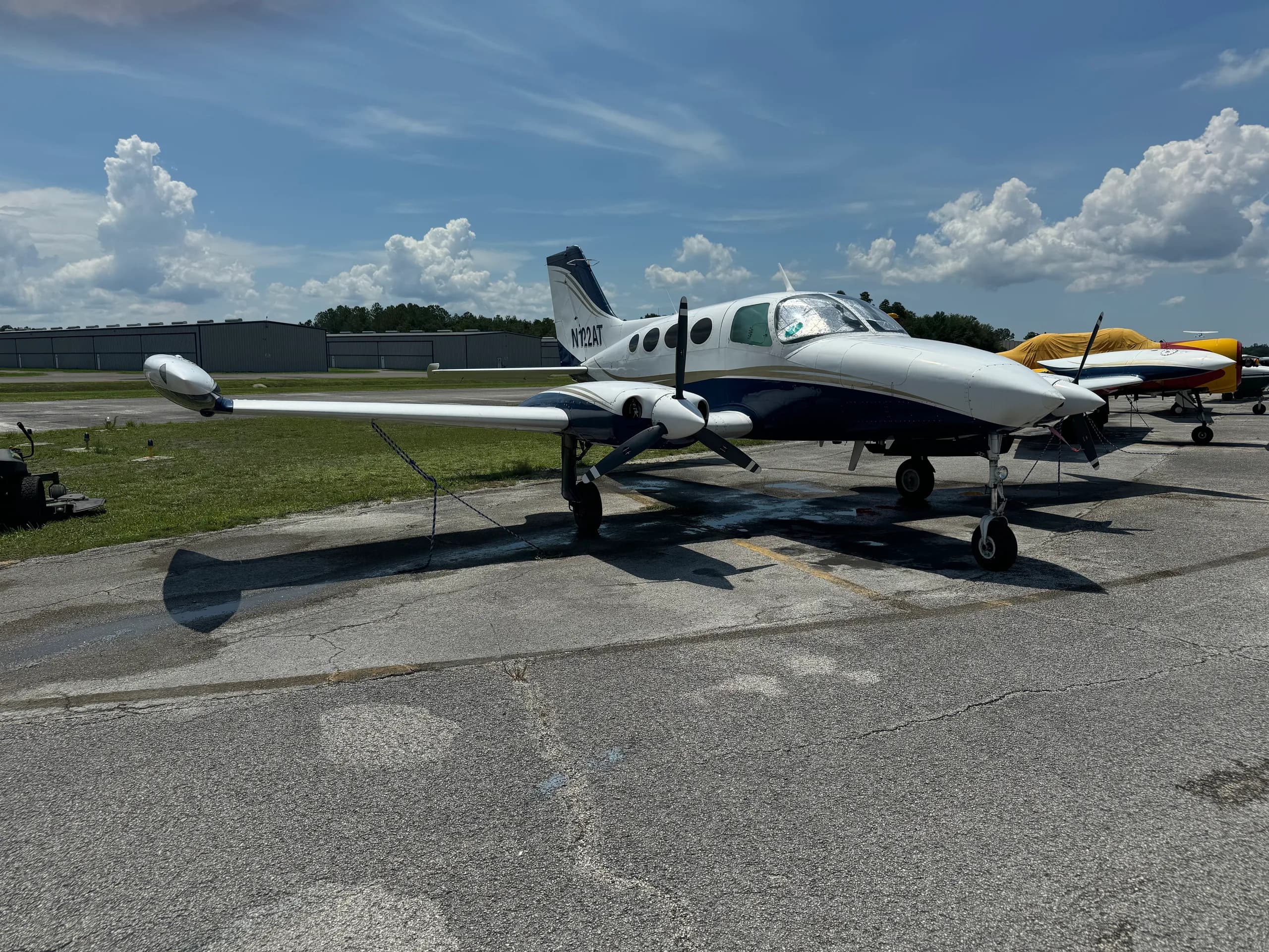 A white and blue Cessna 401 (or similar twin-engine prop) aircraft, registration N122AT, parked on an airport ramp with hangars in the background.
