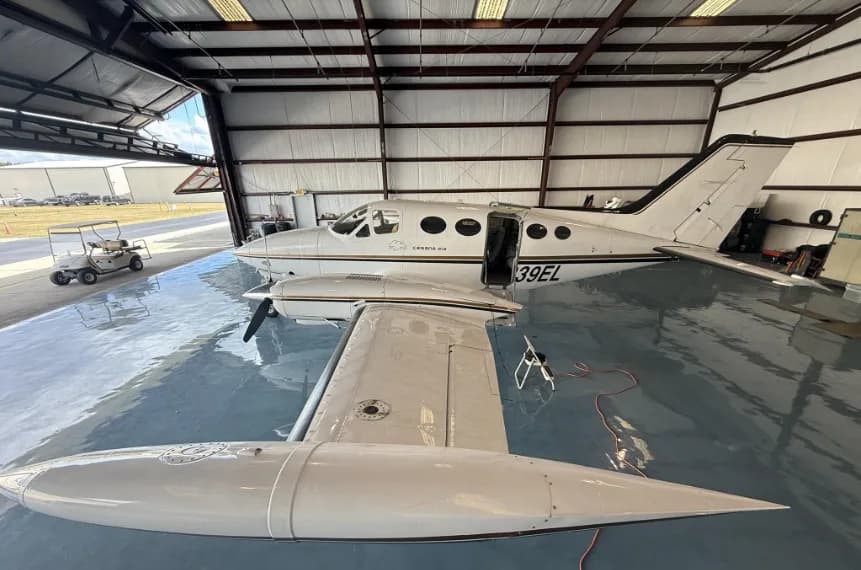 A white Cessna 414 aircraft with registration N239EL, parked in a hangar with its door open, showing the exterior.