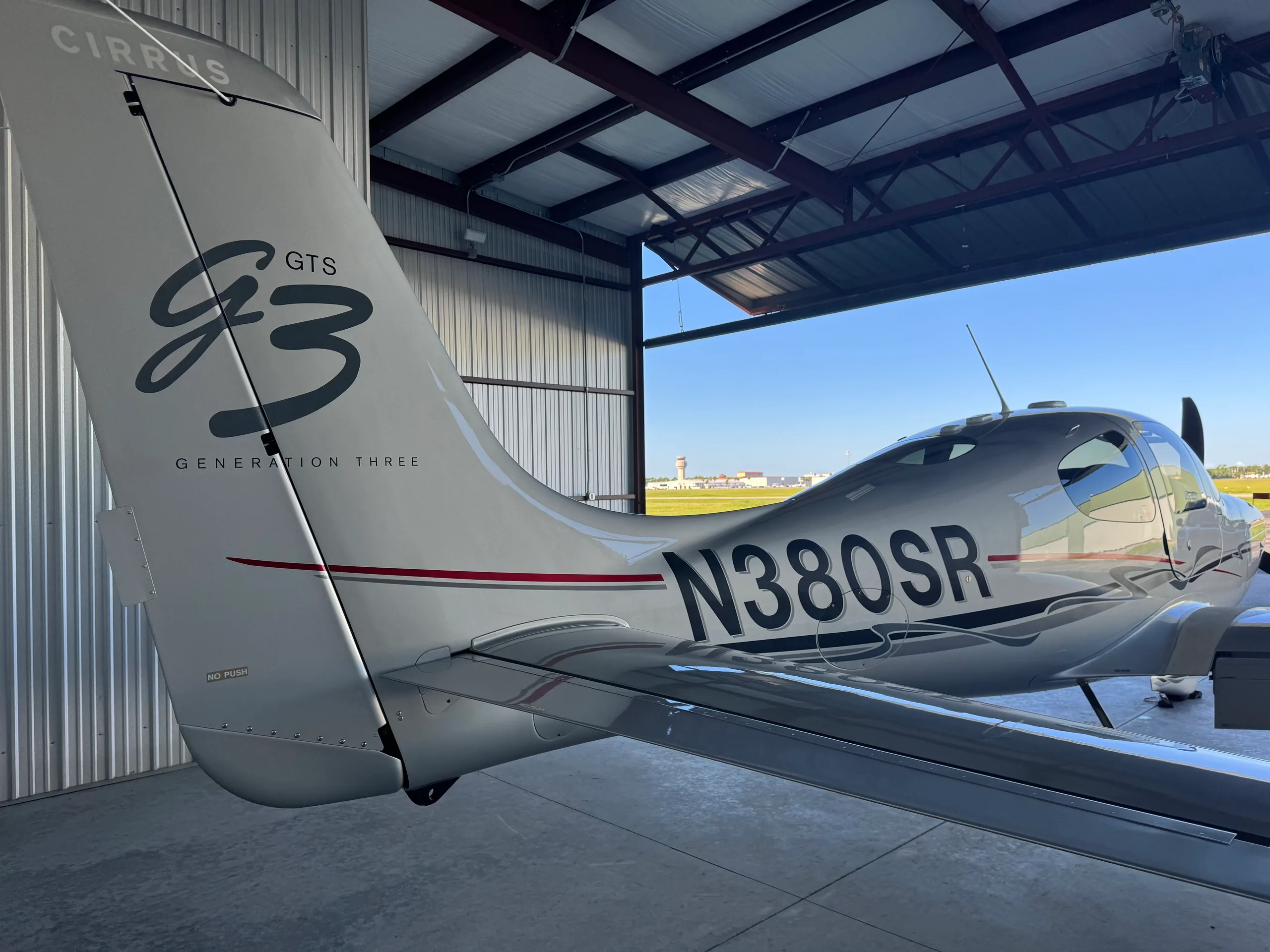 A silver Cirrus SR22 Generation Three aircraft with N380SR registration is parked in a hangar, viewed from the rear-right.
