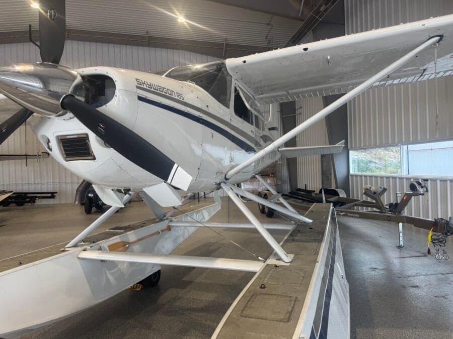 A Skywagon 185 floatplane is parked inside a hangar.