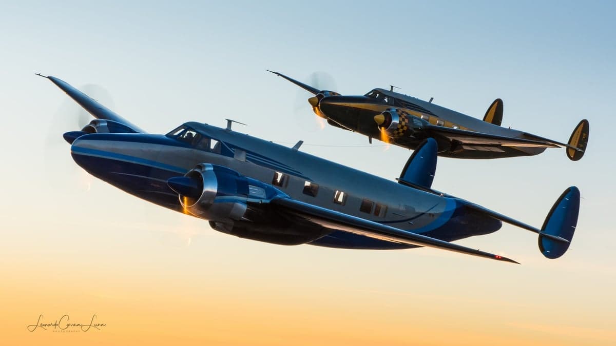 Two Beechcraft Model 18 aircraft flying in formation against a clear sky.