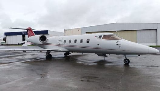 A Learjet aircraft is parked on the tarmac in front of a hangar on a cloudy day.