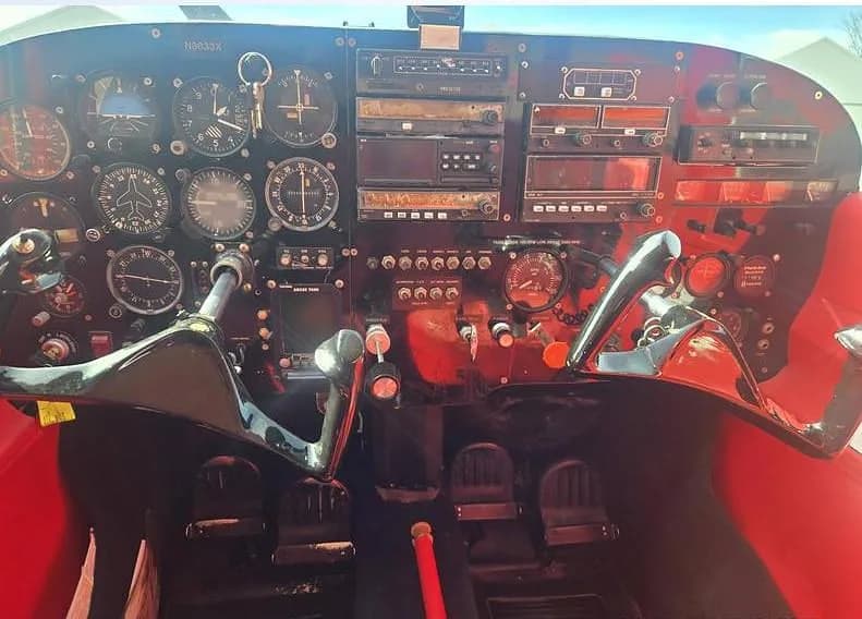 The cockpit of a red aircraft, showing the instrument panel with various gauges and two control yokes.