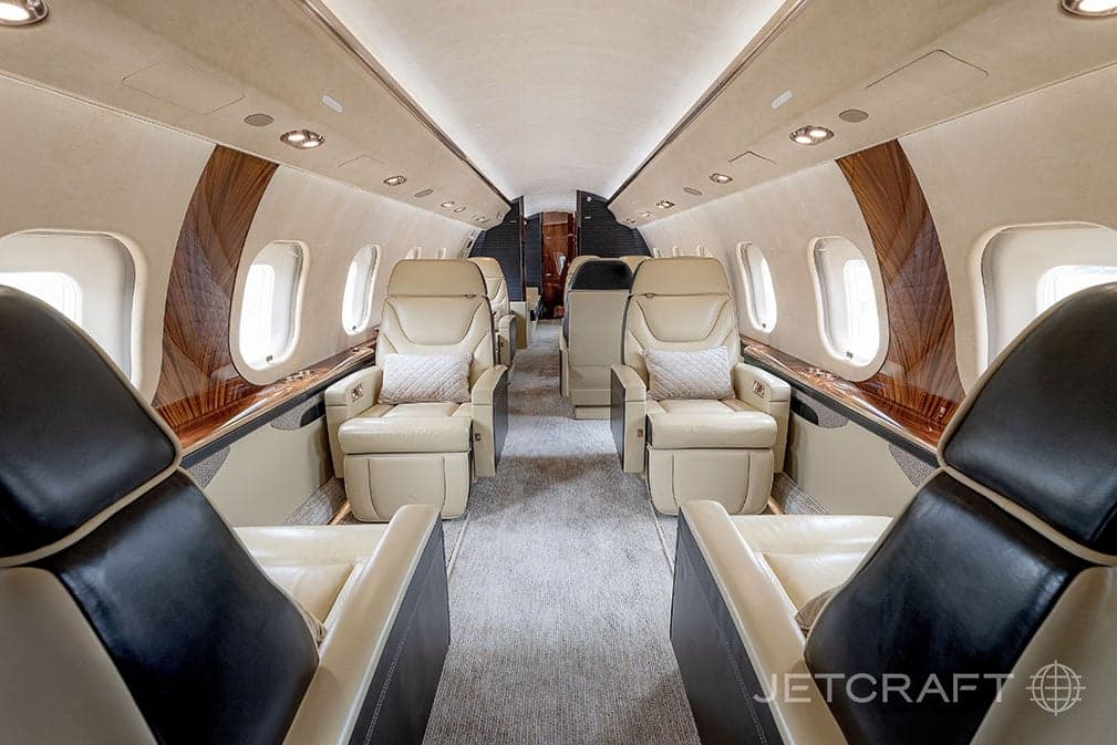 Forward view of the aircraft cabin with tan leather seats and wood trim.