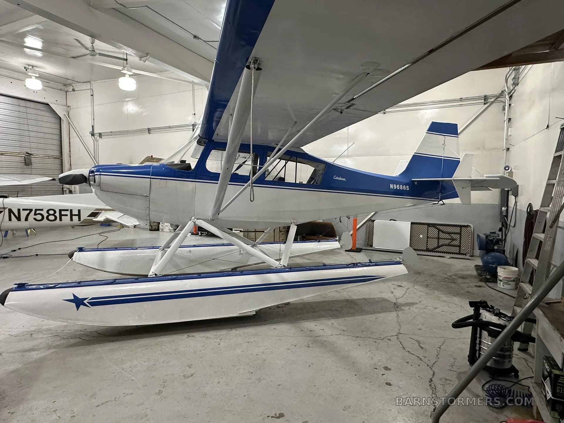 A blue and white Citabria floatplane with registration N9686S is parked in a hangar, viewed from the left side.
