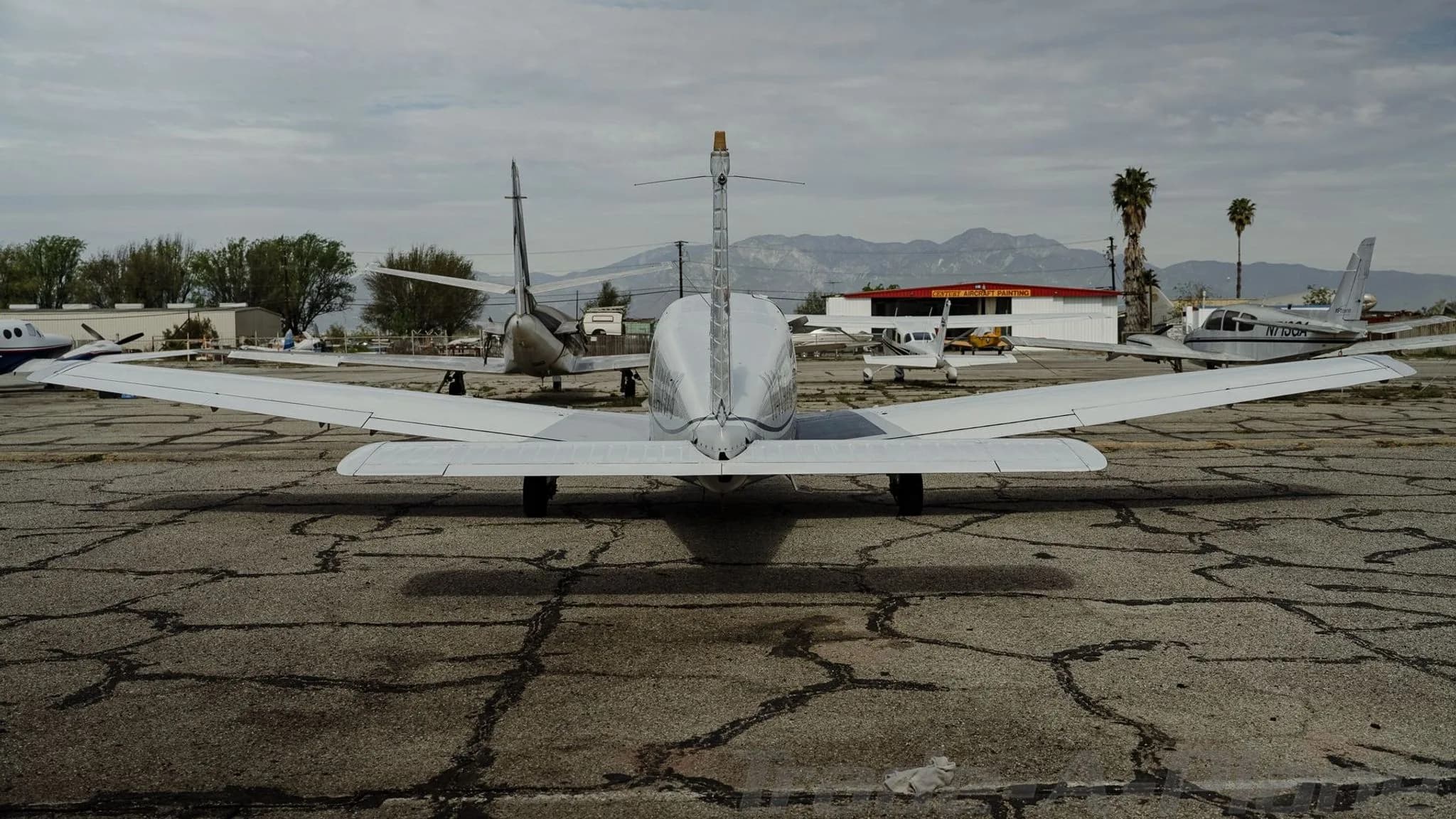 Rear view of a white Piper Cherokee N41978 parked on a cracked tarmac with mountains in the background.