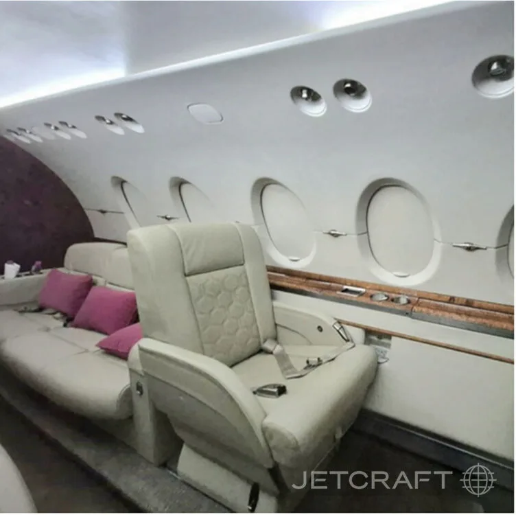 A side view of a private jet cabin, showing light-colored leather seats, a sofa, and multiple oval windows.