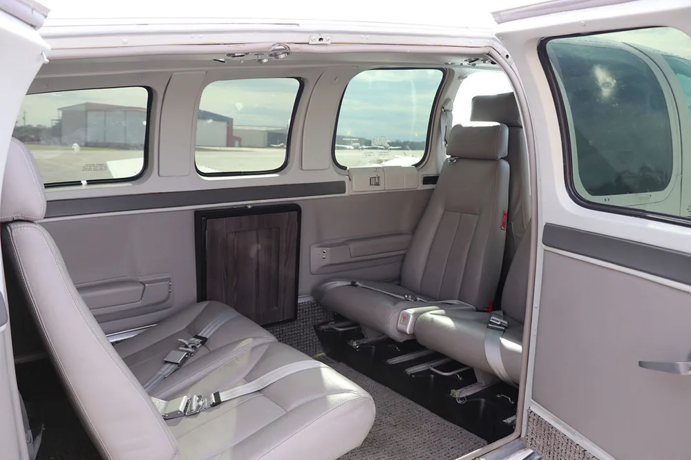 A view of the light gray interior cabin of a Beechcraft Baron 58, showing two rows of seats.