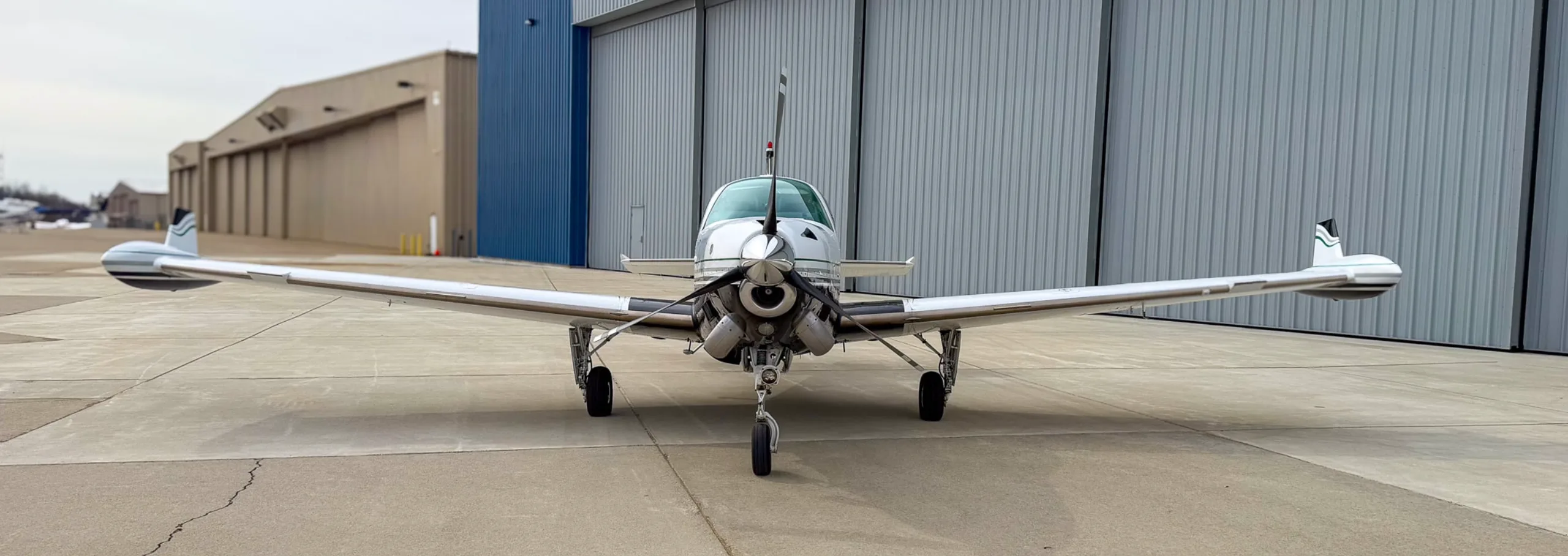 A head-on view of the white and black Beechcraft Baron N157BA, parked on an airfield with hangars in the background.