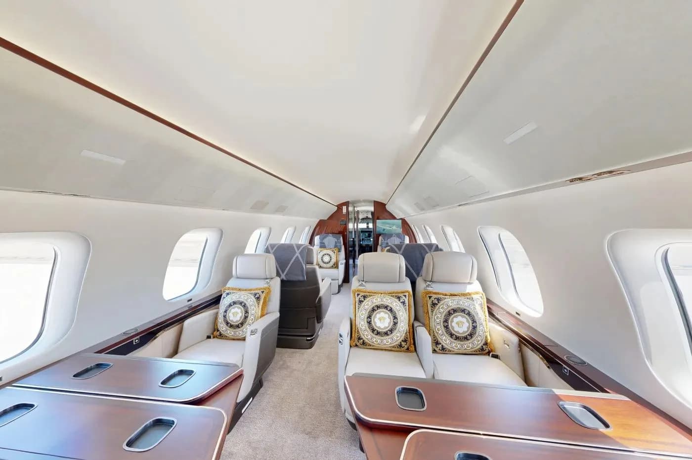A wide view of the private jet's cabin, showing multiple cream leather seats with decorative pillows and dark wood tables.