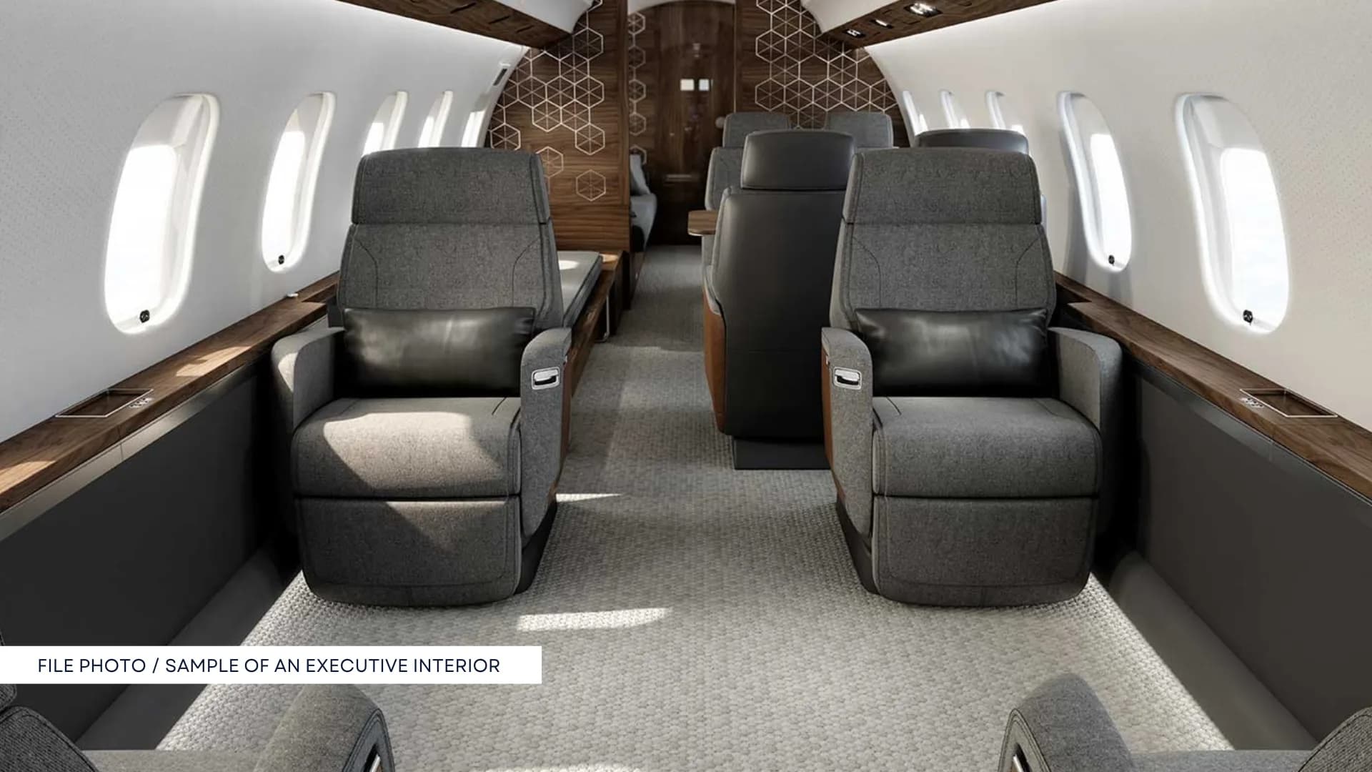 A luxurious aircraft cabin interior with grey upholstered seats, dark wood accents, and large oval windows.