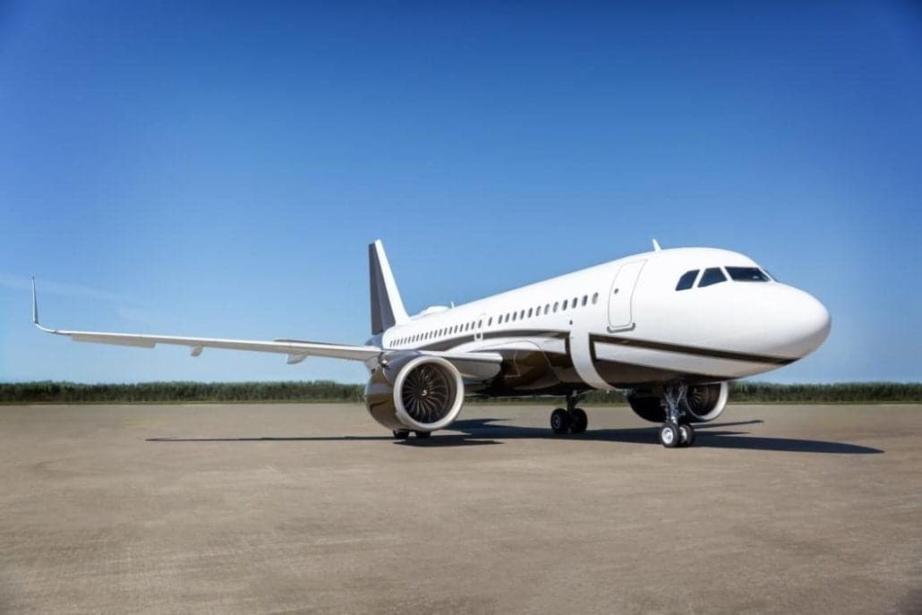 A sleek white and black passenger jet parked on an empty tarmac under a clear blue sky.