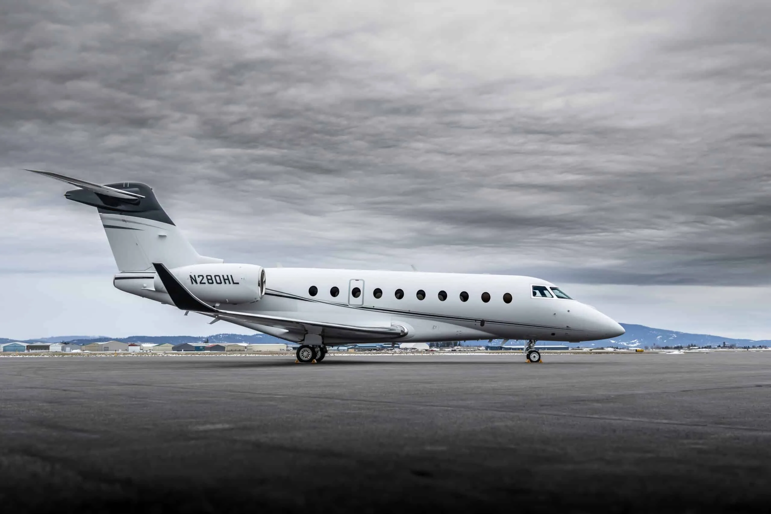 A side view of the white Gulfstream G550 (or similar large business jet) N280HL parked on a tarmac with a cloudy sky.