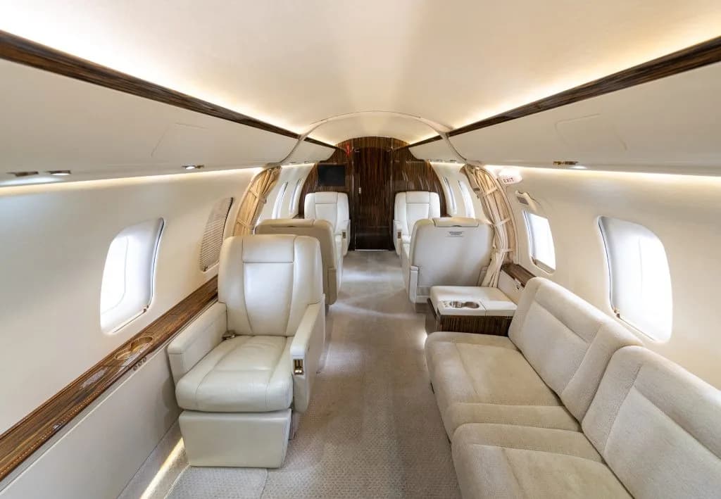 The luxurious interior cabin of a business jet with cream leather seats and dark wood paneling.