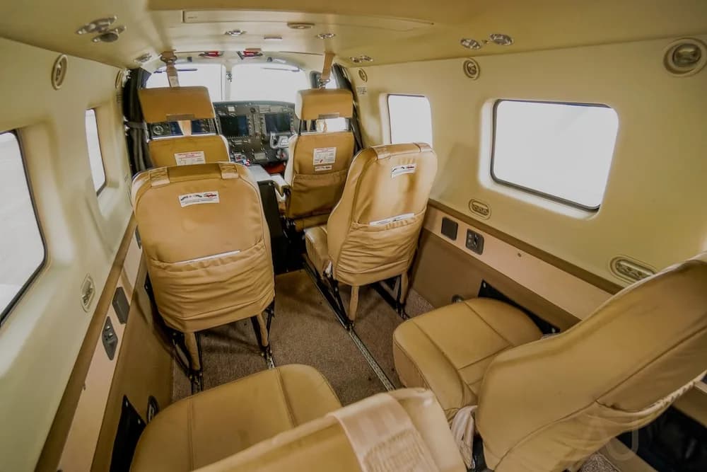 The aircraft interior cabin with tan seats, showing the aisle and a glimpse of the cockpit.
