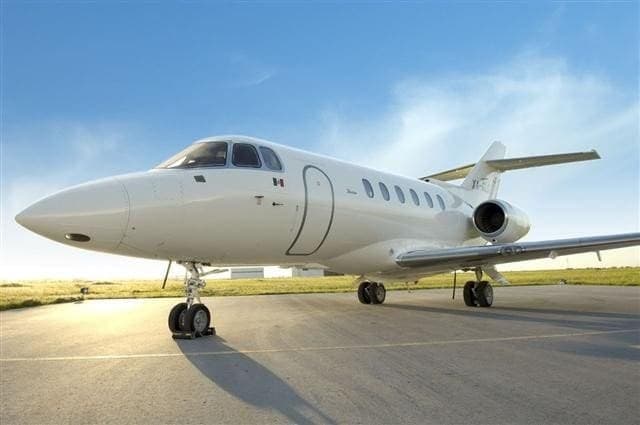 A white Dassault Falcon business jet is parked on the tarmac.