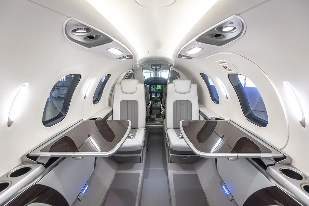 The interior cabin of a HondaJet HA-420, showing white and grey leather seats with fold-out tables deployed.