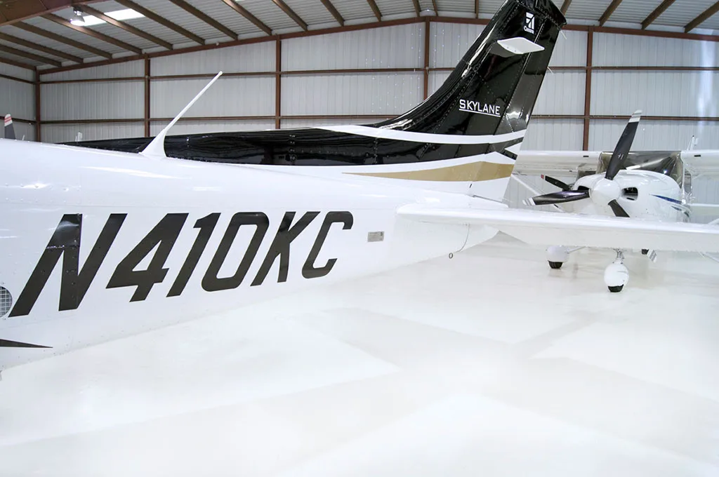 A close-up view of the tail section of a white Cessna Skylane aircraft with black and gold stripes, showing the N-number.
