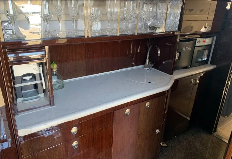 A well-appointed aircraft galley featuring a sink, coffee machines, and crystal glassware stored above a dark wood counter.