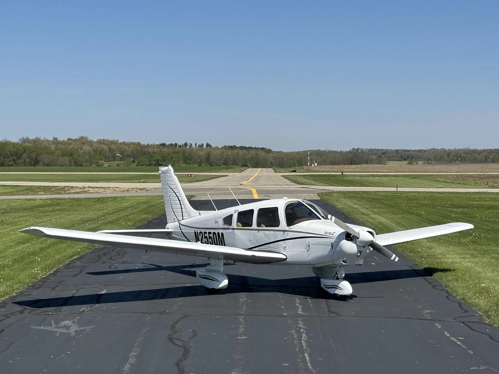A white Piper Cherokee aircraft, N2550M, with black stripes, parked on an asphalt runway under a clear blue sky.
