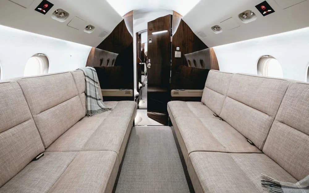 The aft cabin interior of a Dassault Falcon 900EX, featuring two opposing beige fabric divans with a plaid blanket.
