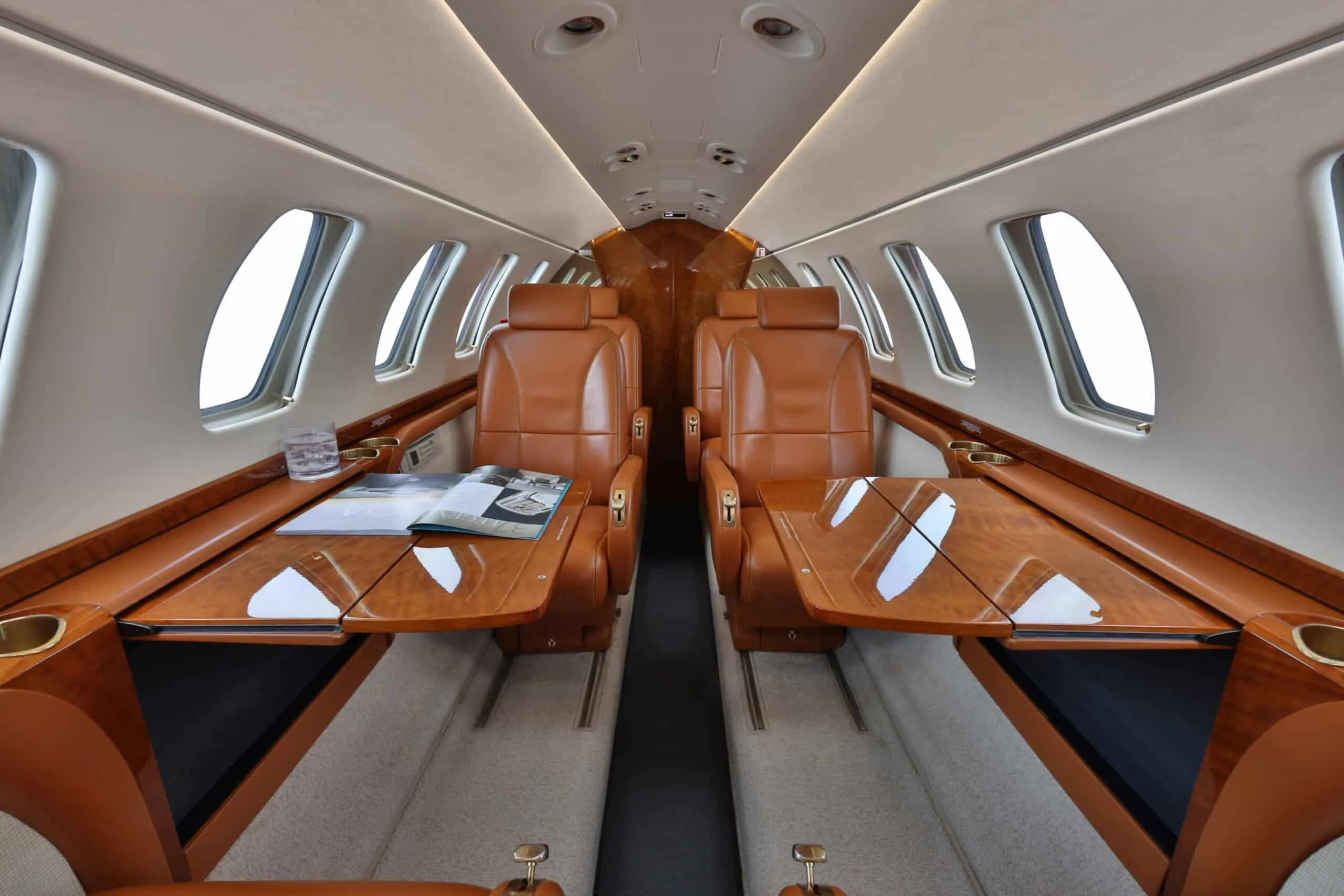 Private jet cabin interior with tan leather seats and two polished wooden tables deployed.