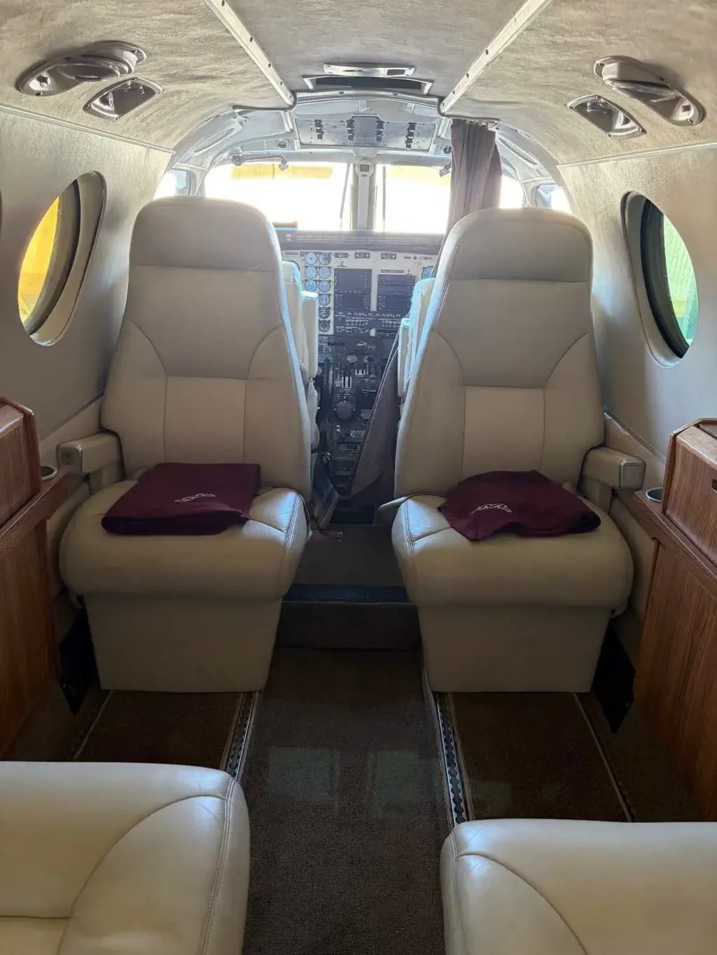The interior cabin of a Beechcraft King Air C90, showing two beige leather seats facing forward towards the cockpit.