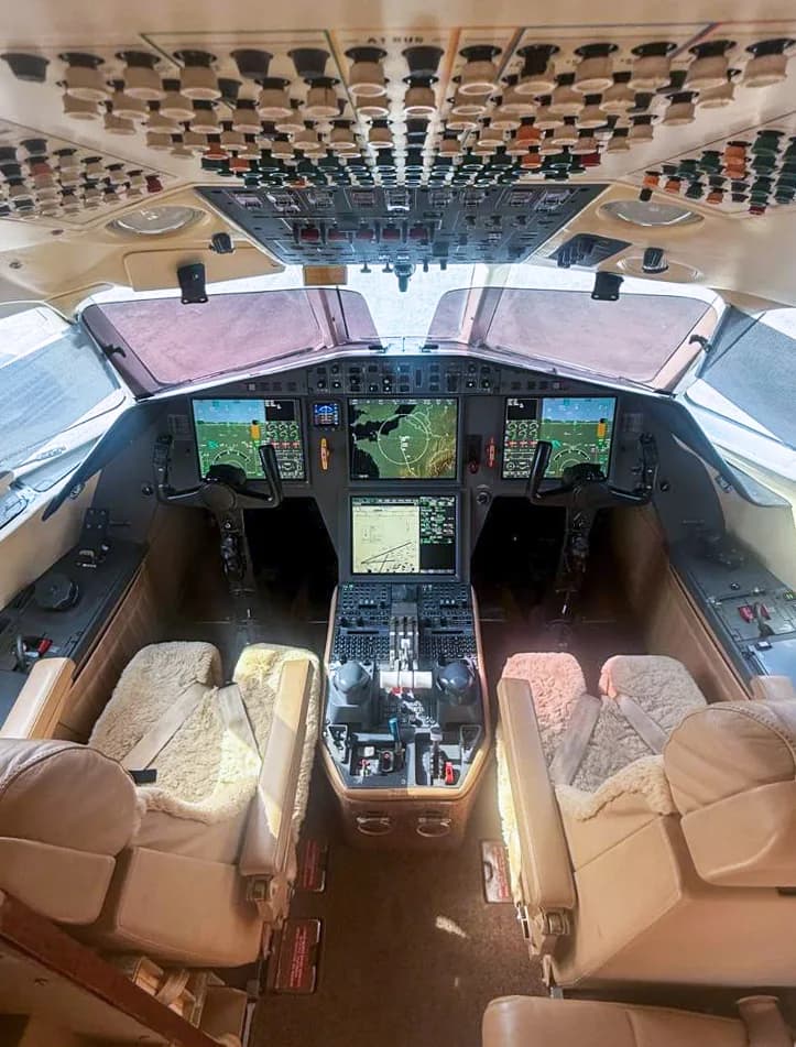 The cockpit of a modern business jet, featuring multiple digital displays, control yokes, and an overhead panel.
