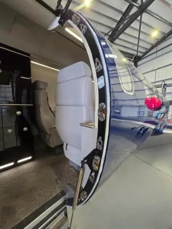 A dark blue Learjet is parked inside a hangar, with red engine covers.