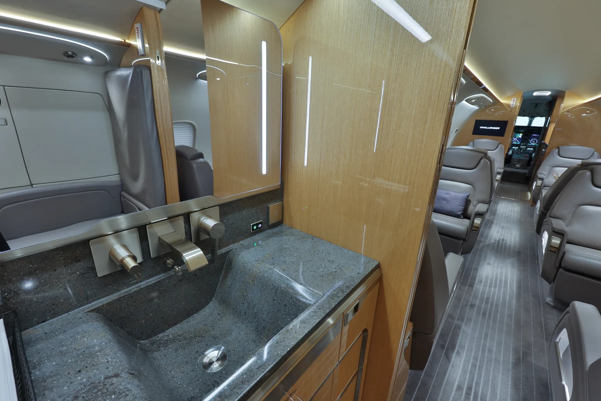 The lavatory of a Challenger aircraft with a sink and mirror, looking into the cabin.