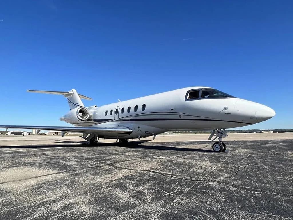 A white business jet with dark blue stripes is parked on an asphalt tarmac, viewed from the front-left.