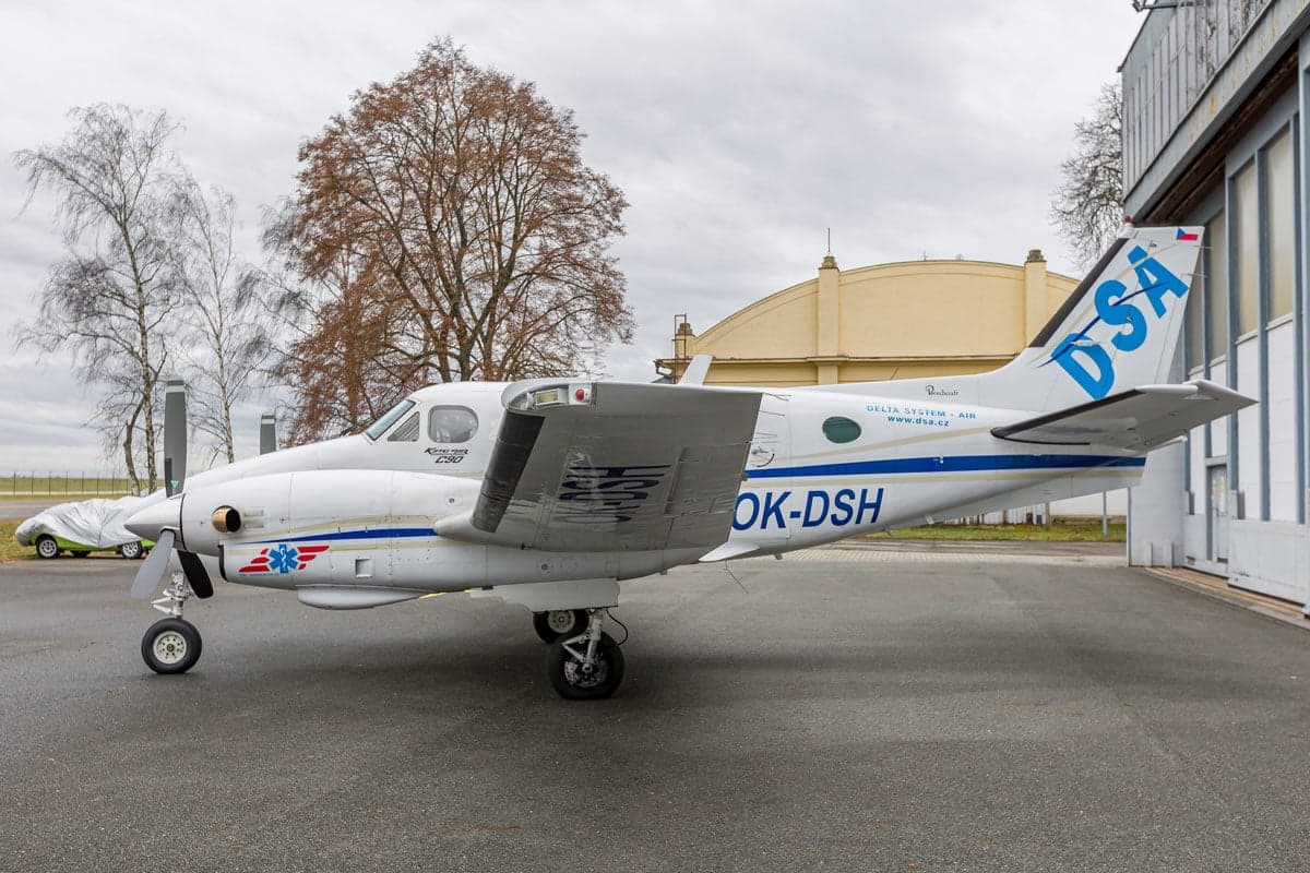 Side view of a Beechcraft King Air C90 aircraft with a white and blue paint scheme, parked on the tarmac.