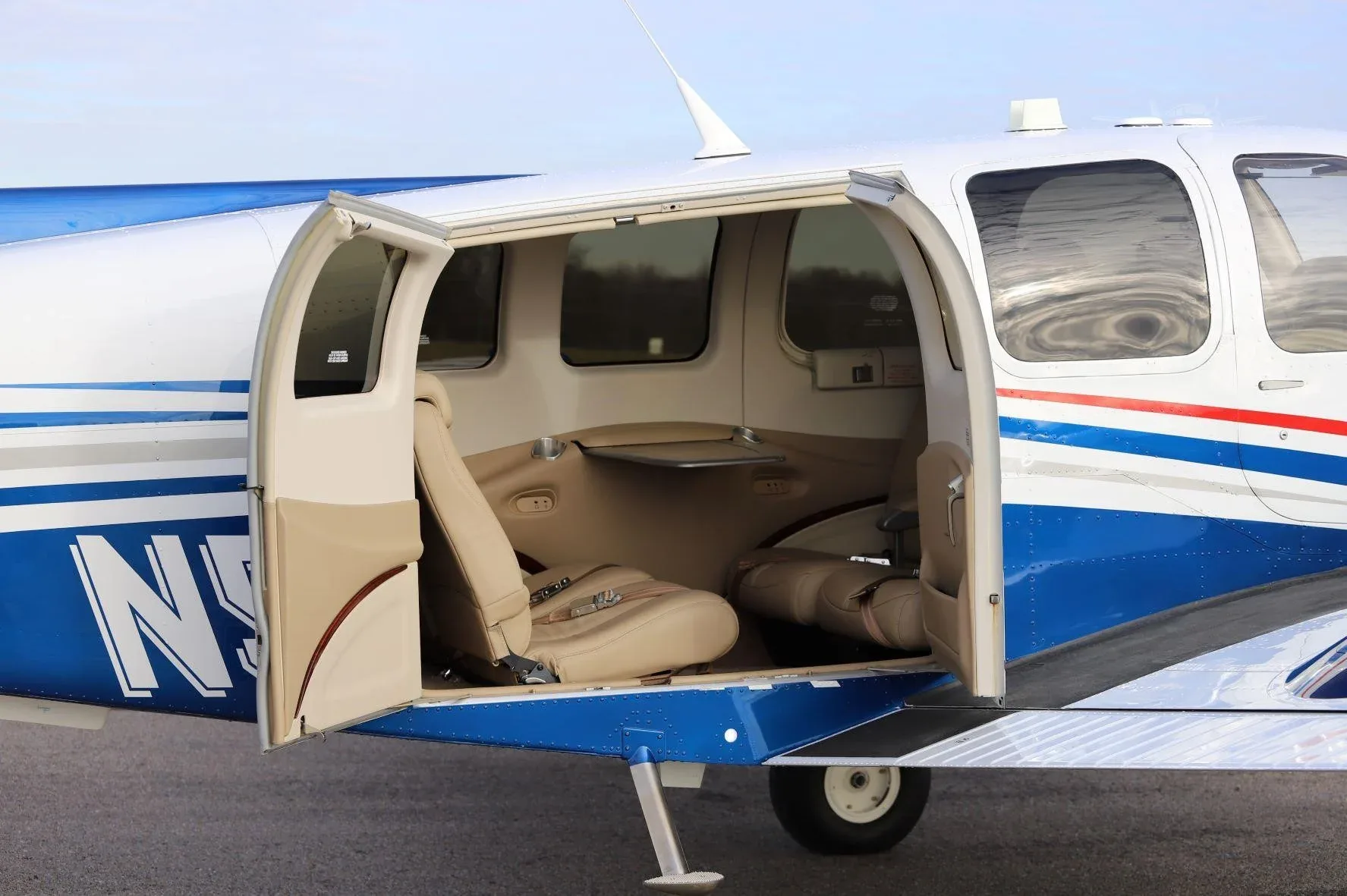 The tan leather interior cabin of a white and blue Beechcraft Baron G58, viewed through the open passenger door.