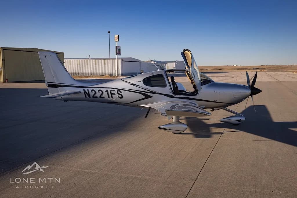 A side view of the silver Cirrus SR22T aircraft N221FS with its doors open, parked on an airfield.